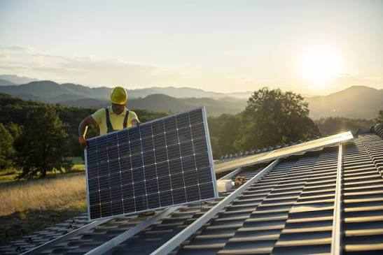 Ouvrier qui pose un panneaux solaire sur une toiture en tuile noire