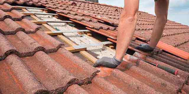 ouvrier qui répare une toiture à tuile rouge